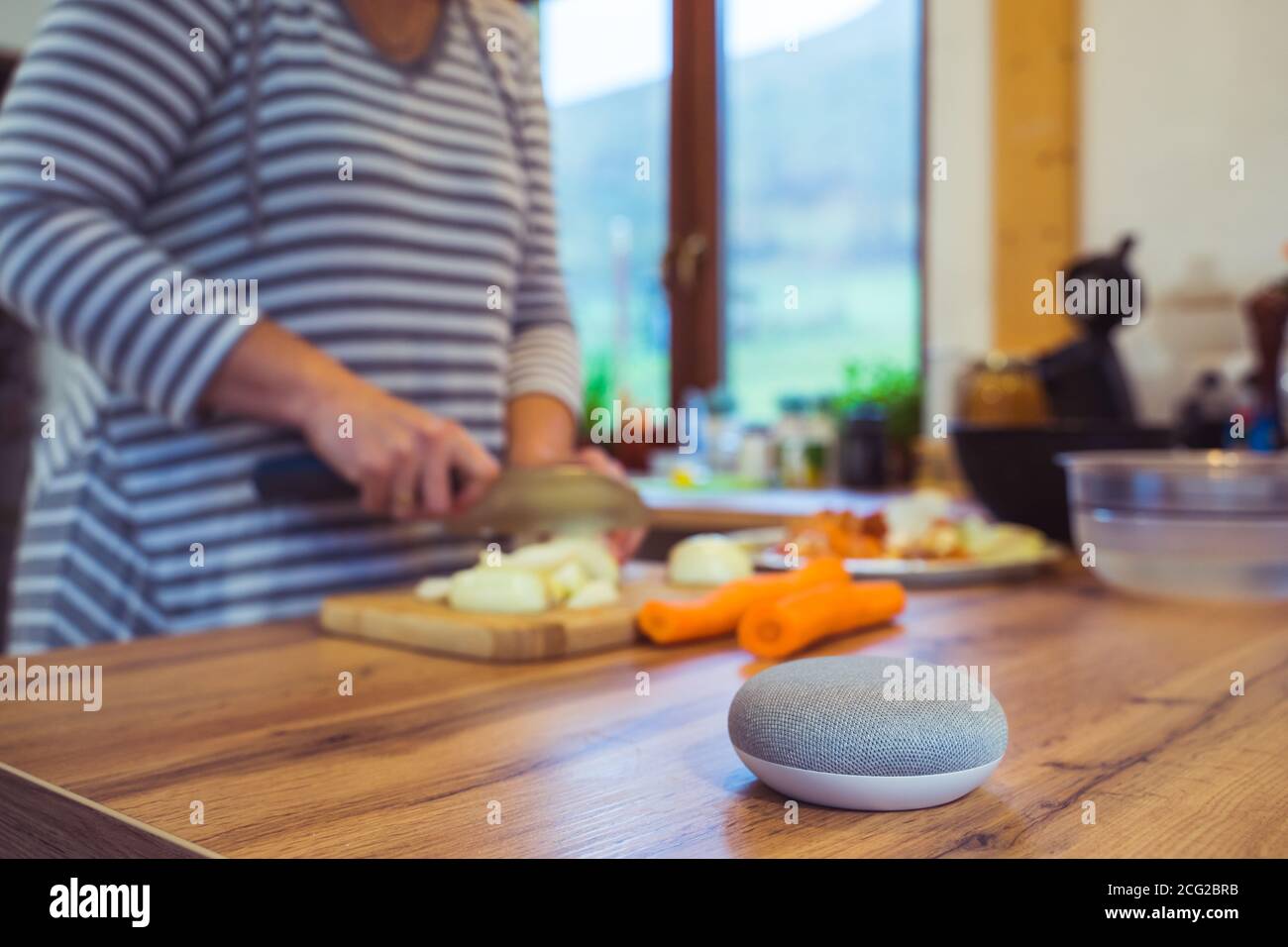 Sprachgesteuerter Smart Speaker in einem Zuhause mit Sprachsteuerung Smart Speaker in einer Innenraumumgebung mit einer Frau Kochen im Hintergrund Stockfoto