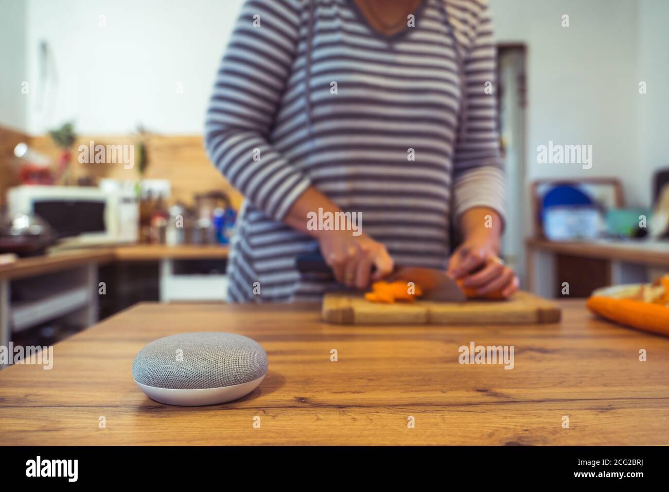Sprachgesteuerter Smart Speaker in einem Zuhause mit Sprachsteuerung Smart Speaker in einer Innenraumumgebung mit einer Frau Kochen im Hintergrund Stockfoto