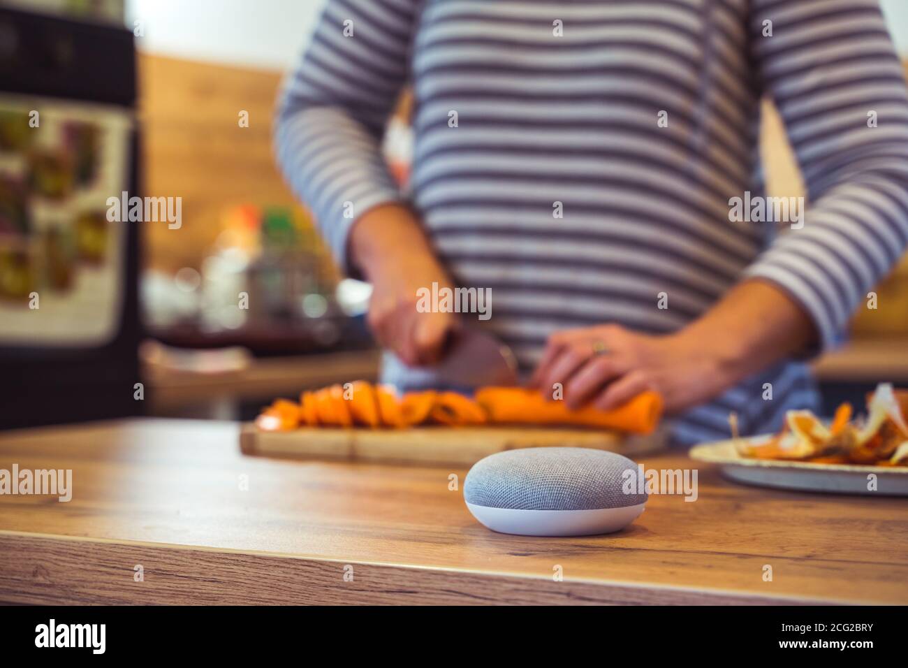 Sprachgesteuerter Smart Speaker in einem Zuhause mit Sprachsteuerung Smart Speaker in einer Innenraumumgebung mit einer Frau Kochen im Hintergrund Stockfoto