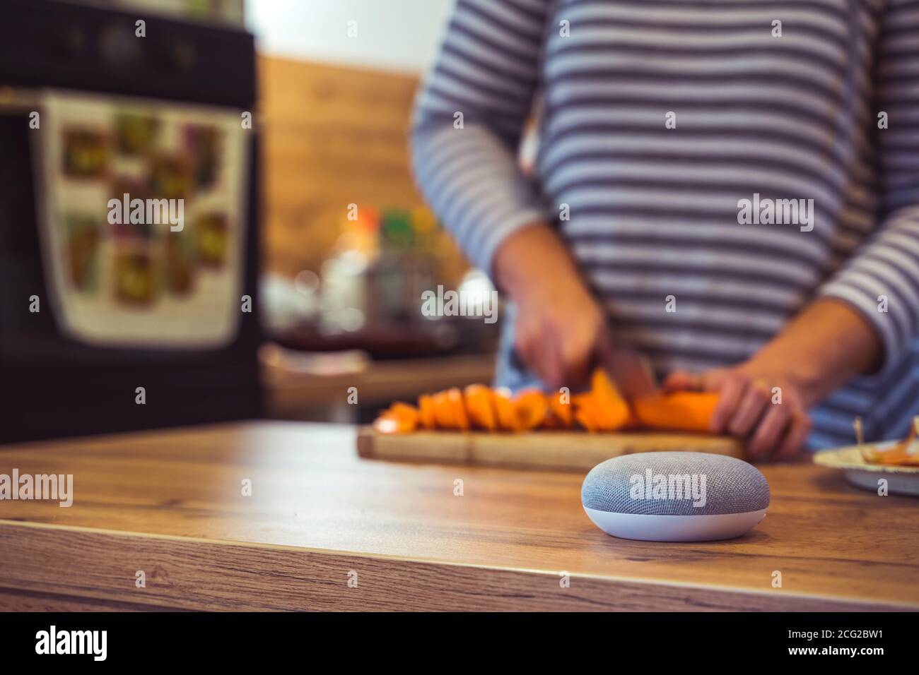 Sprachgesteuerter Smart Speaker in einem Zuhause mit Sprachsteuerung Smart Speaker in einer Innenraumumgebung mit einer Frau Kochen im Hintergrund Stockfoto