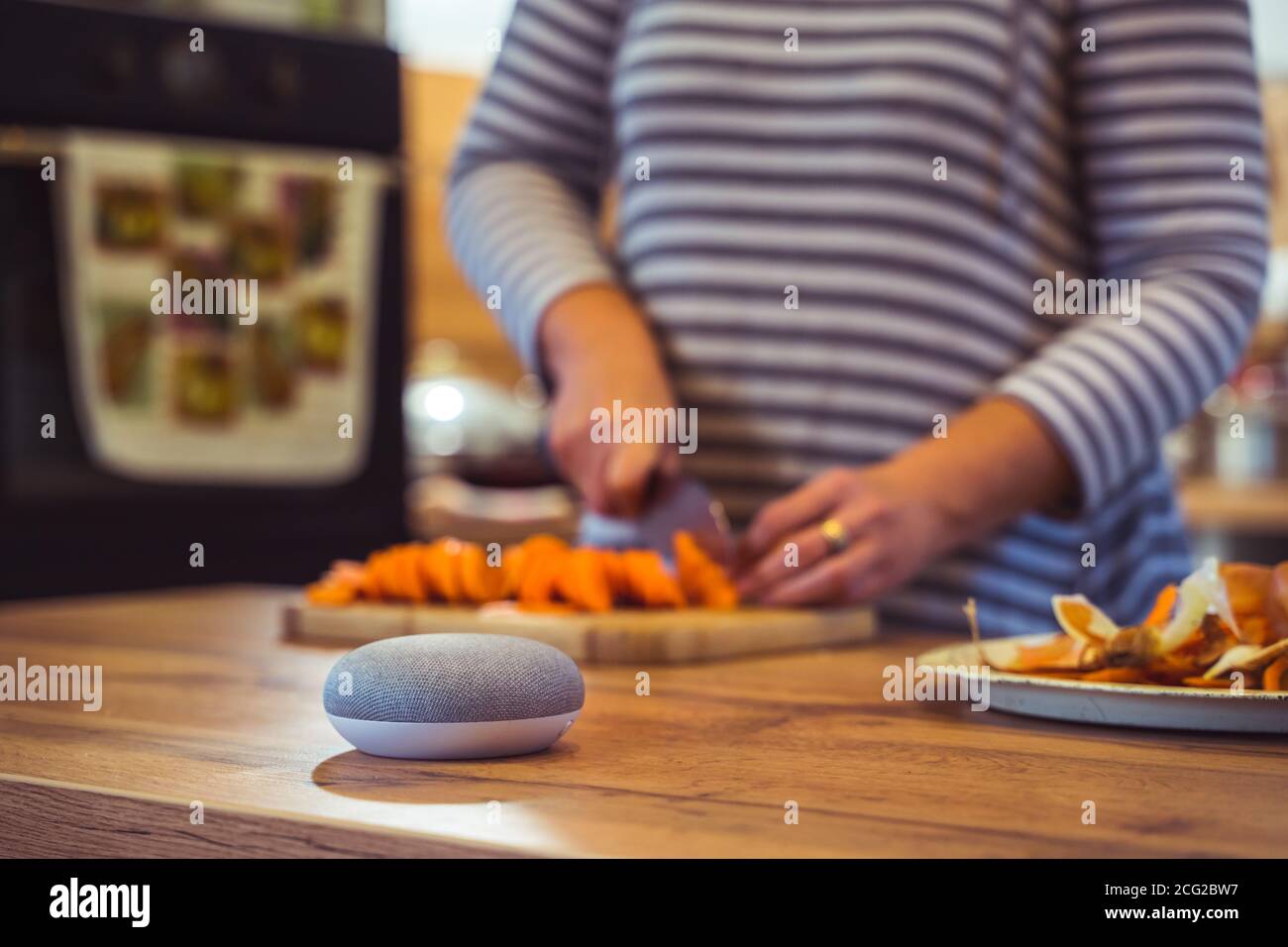 Sprachgesteuerter Smart Speaker in einem Zuhause mit Sprachsteuerung Smart Speaker in einer Innenraumumgebung mit einer Frau Kochen im Hintergrund Stockfoto