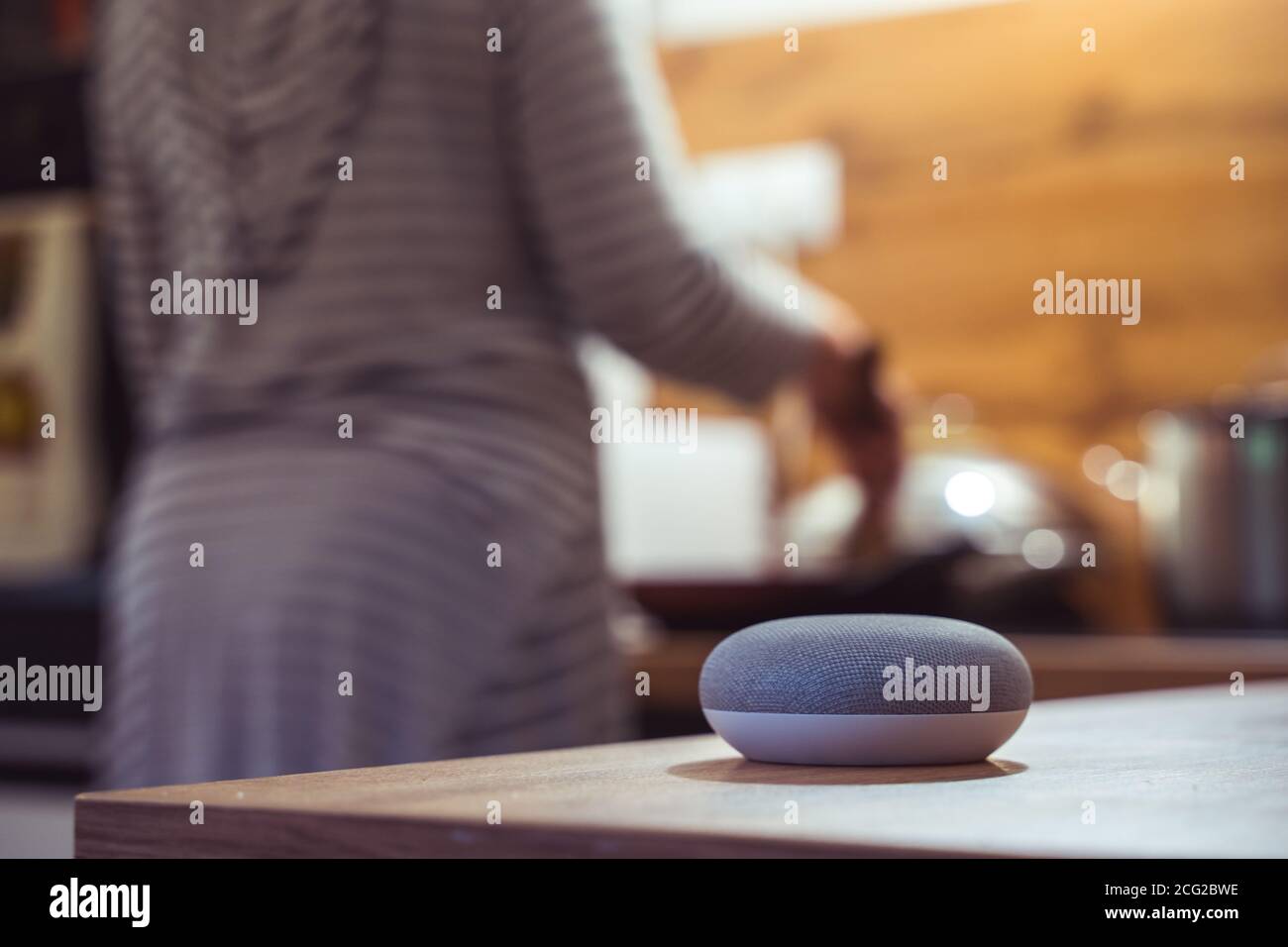 Sprachgesteuerter Smart Speaker in einem Zuhause mit Sprachsteuerung Smart Speaker in einer Innenraumumgebung mit einer Frau Kochen im Hintergrund Stockfoto