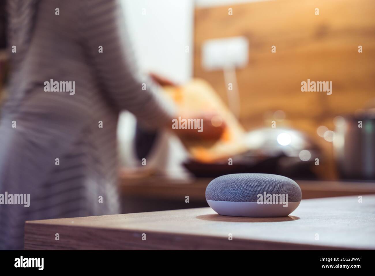 Sprachgesteuerter Smart Speaker in einem Zuhause mit Sprachsteuerung Smart Speaker in einer Innenraumumgebung mit einer Frau Kochen im Hintergrund Stockfoto