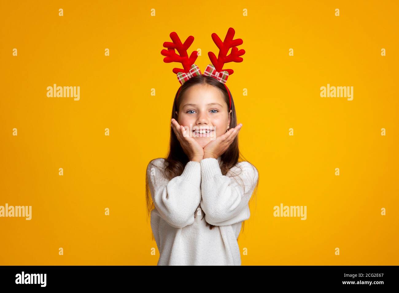 Weihnachtszeit. Cute Vorschule Mädchen mit Hörnern in Pullover setzt ihre Hände auf Wangen Stockfoto