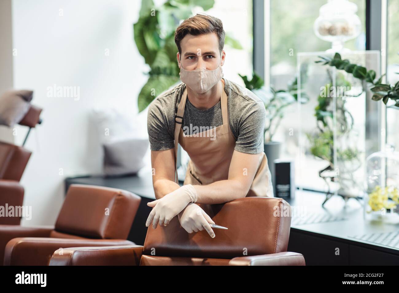 Junge männliche Friseur in Schutzmaske wartet auf Kunden im Salon Interieur, freien Raum Stockfoto