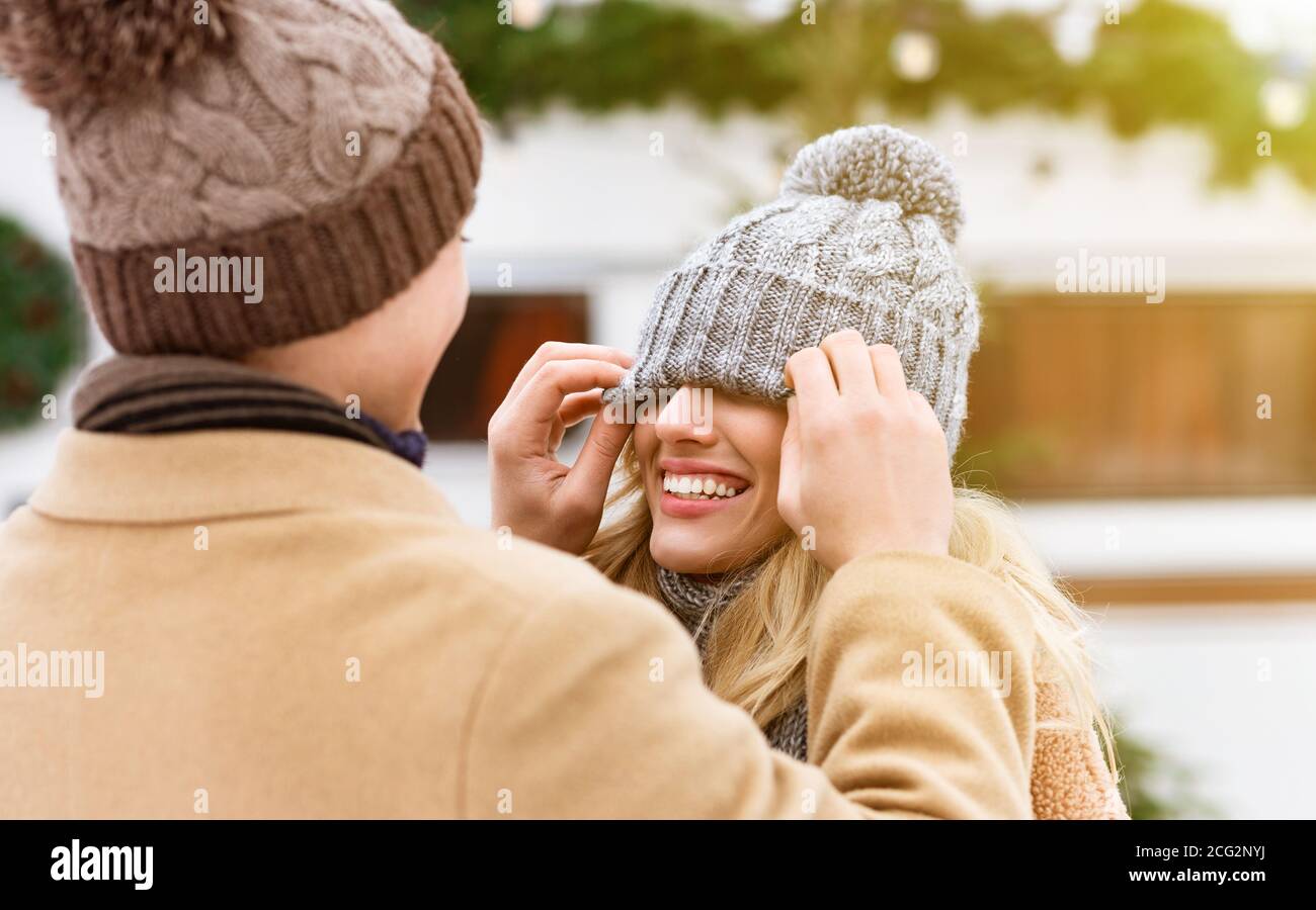 Kerl, der die Augen der Freundin mit Hut bedeckt, während er Spaß im Freien hat Gemeinsam im Winter Stockfoto