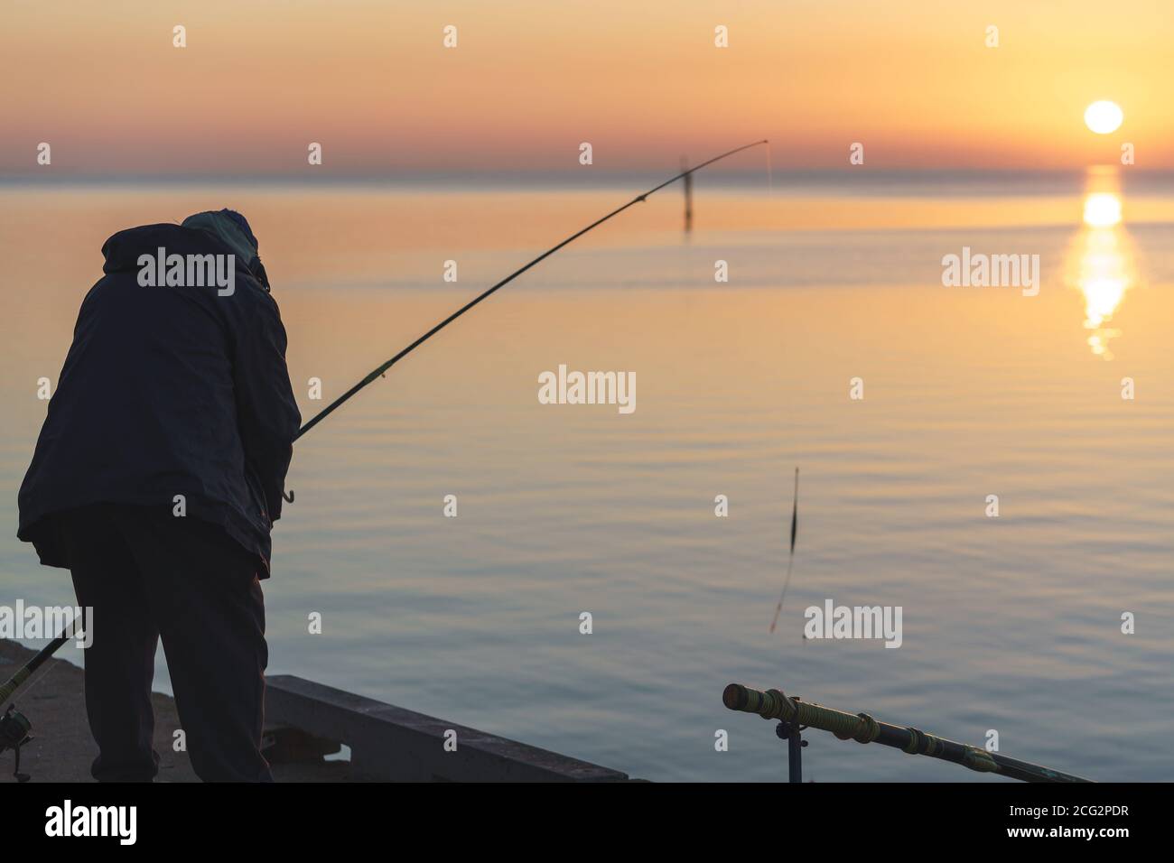 Silhouette eines erwachsenen Mannes, der am Pier Geelong angeln soll Beruhigendes Meer mit Sonnenaufgang während der goldenen Stunde Stockfoto