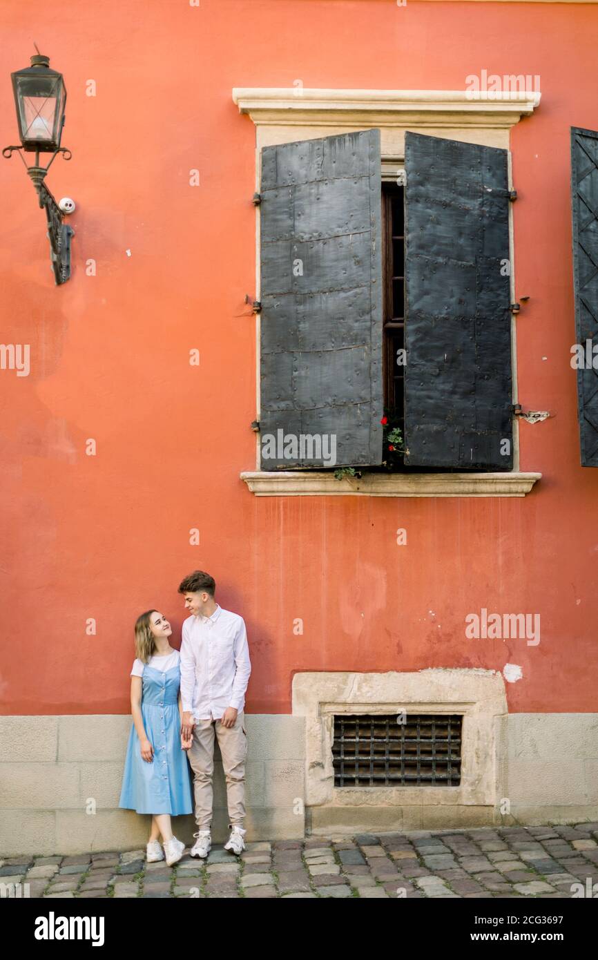 Porträt eines verliebten Paares in der Nähe eines alten orangefarbenen Gebäudes. Glücklicher Mann und Mädchen in blauem Kleid, auf der Wand des alten Gebäudes und lehnte Stockfoto