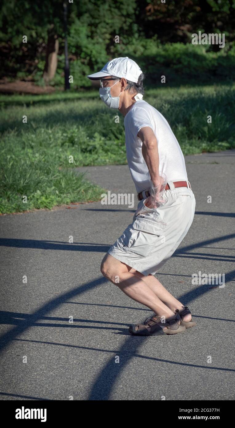 Ein flink älterer Bürger macht tiefe Kniebeugen, die sich für einen Übungsspaziergang aufwärmen. In einem Park in Queens, New York City. Stockfoto