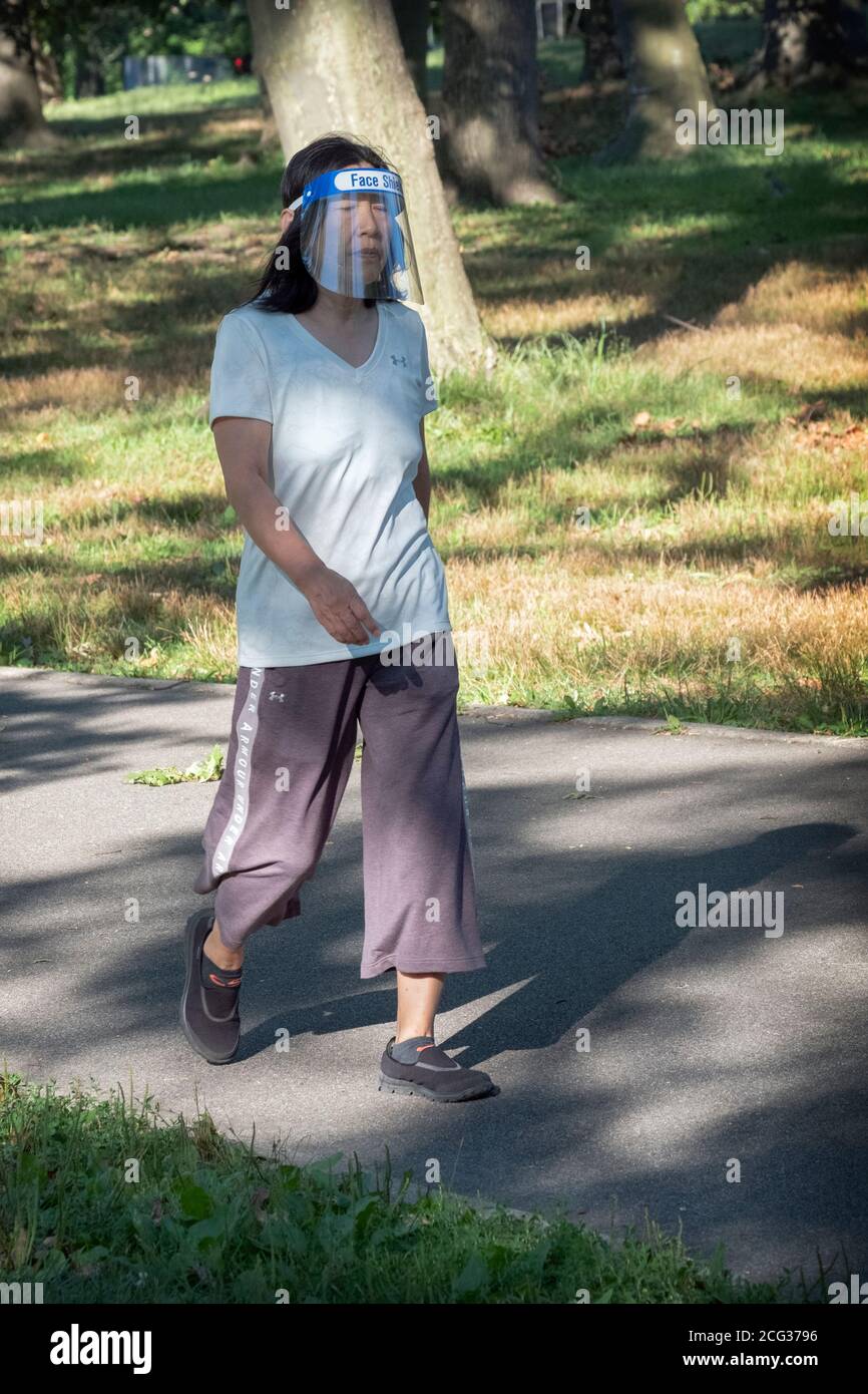 Eine asiatisch-amerikanische Frau auf einem Übungsweg mit Gesichtsschild, aber ohne Maske. Ich habe einen Park in Queens, New York City. Stockfoto