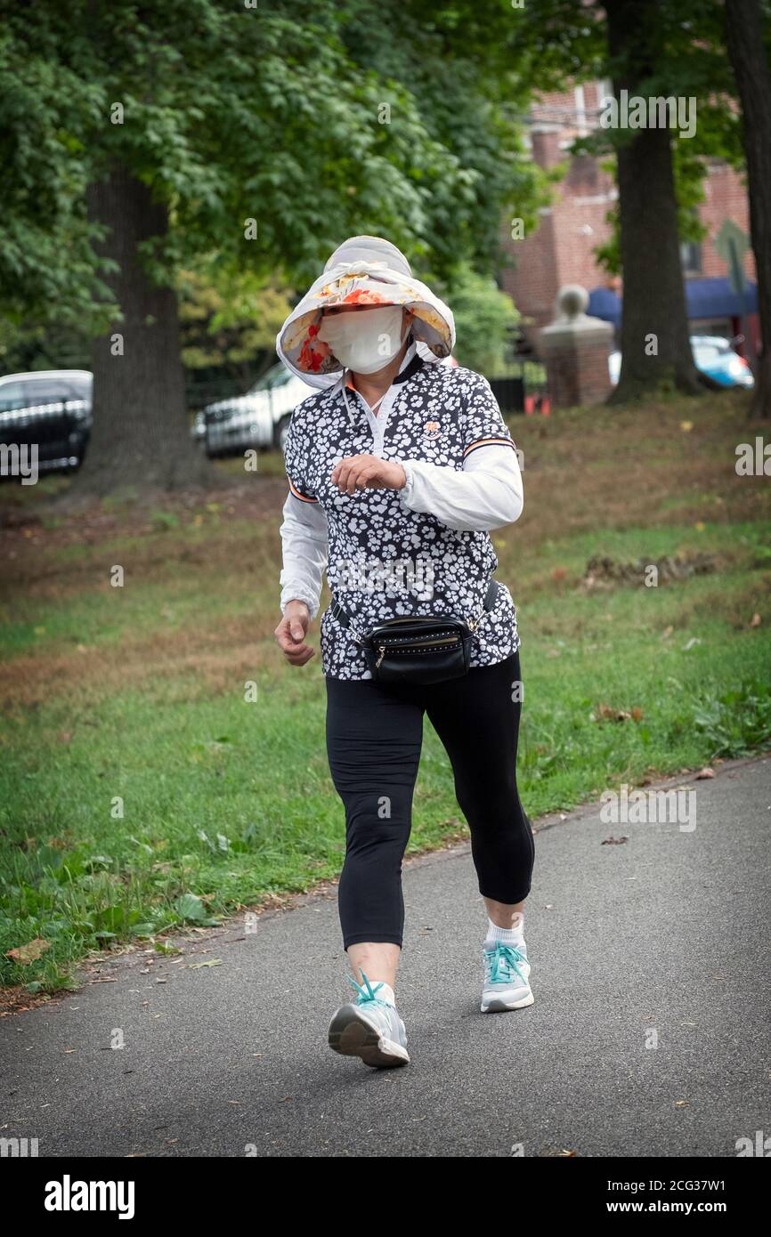 Eine asiatisch-amerikanische Frau, deren Gesicht fast vollständig von ihrer Maske bedeckt ist. Auf einem flotten Übungsspaziergang im Kissenal Park, Flushing, Queens, New York. Stockfoto