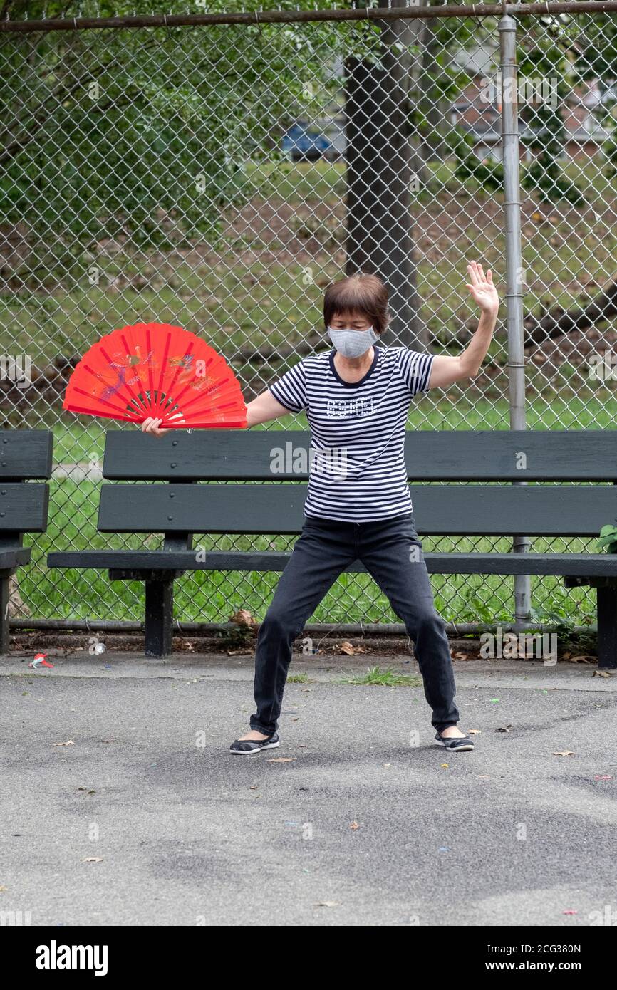 Der Anführer einer Tai Chi Klasse, die rote Faltfächer verwendet. In einem Park in Flushing, Queens, New York City. Stockfoto