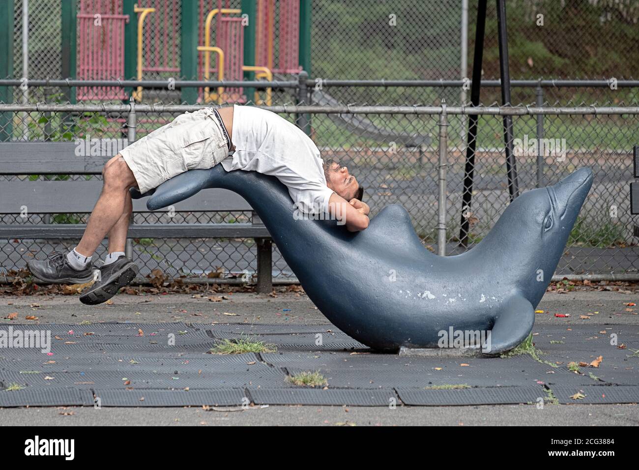 EXTREME DEHNUNG. Auf dem Spielplatz im Kissena Park, Flushing, New York, streckt ein Mann den Rücken über eine Fischstatue. Stockfoto