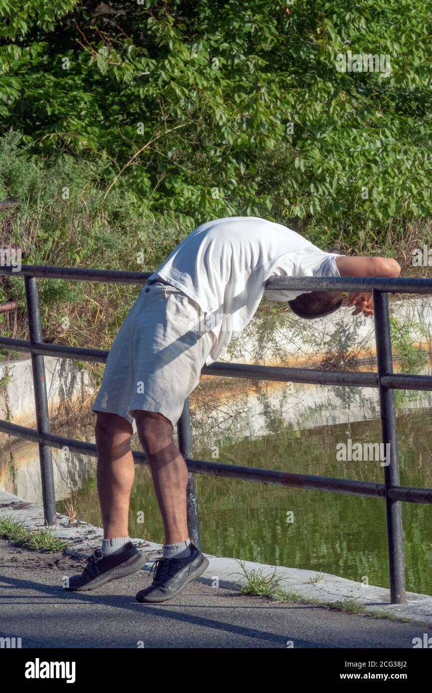 EXTREME DEHNUNG. Ein Mann streckt seinen Rücken über einen Zaun in der Nähe des Sees im Kissena Park, Flushing, New York. Stockfoto