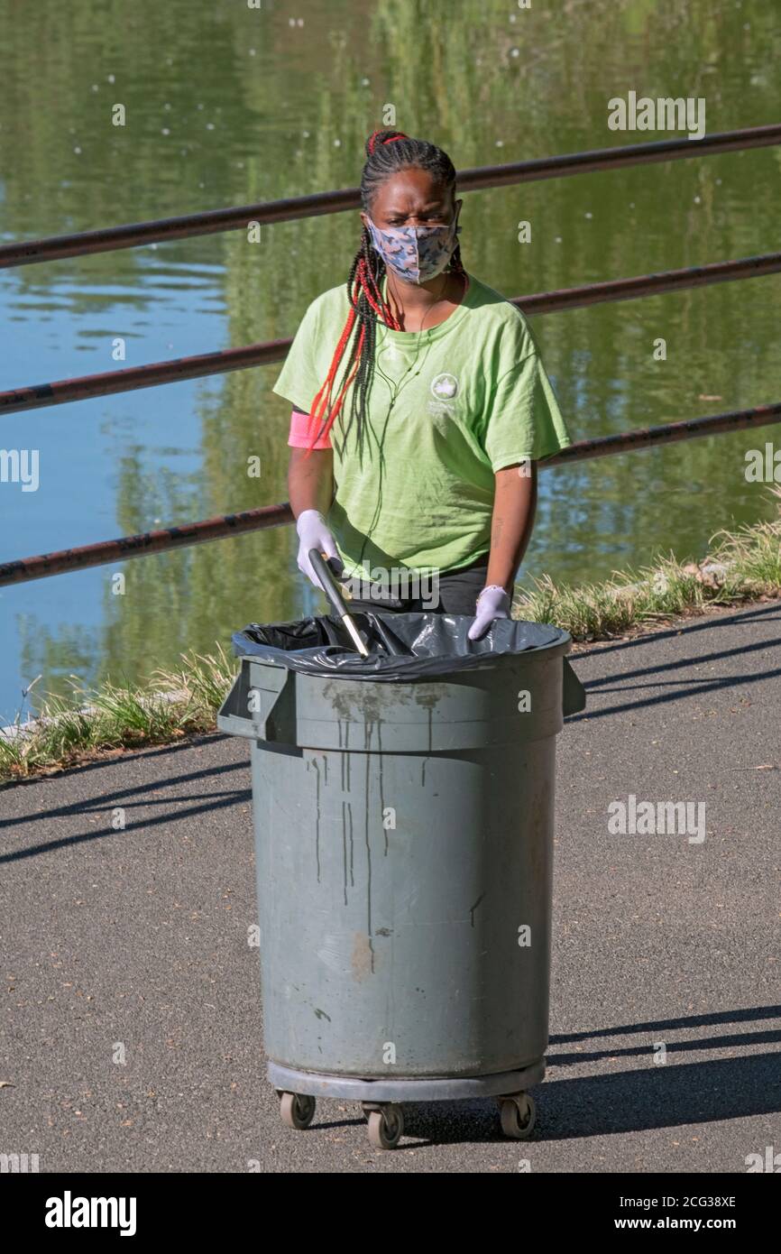 Ein attraktiver Mitarbeiter des Parks Department, der eine OP-Maske und Handschuhe trägt, reinigt die Gegend in der Nähe des Sees in Kissena Park, Flushing, Queens, New York City. Stockfoto
