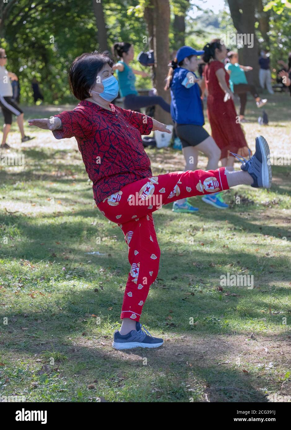 Eine asiatisch-amerikanische Frau mittleren Alters bei einem Outdoor-Tanzkurs ist eine der wenigen, die eine Maske tragen. In einem Park in Queens, New York Stockfoto