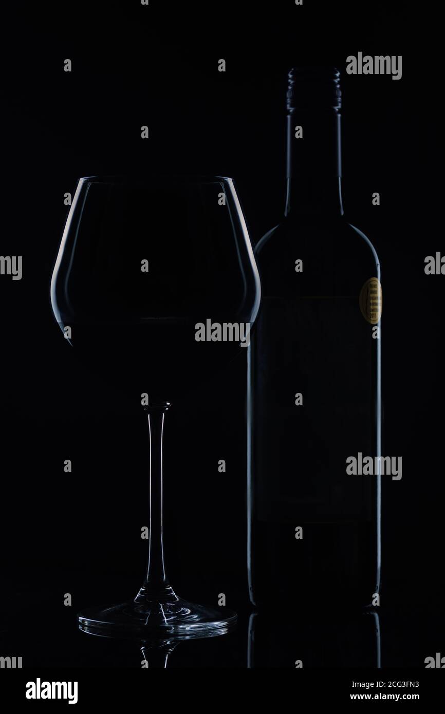 Weinflasche und ein Glas Rotwein im Hintergrund Licht. Dunkle Stimmung Stockfoto