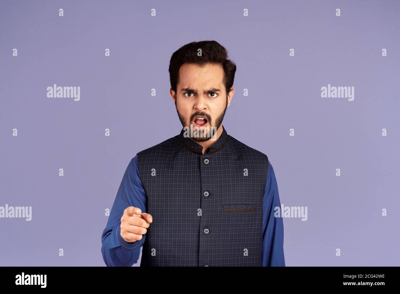 Wütend indischen Kerl zeigt Finger auf Bildschirm in Anklage über Lila Hintergrund Stockfoto