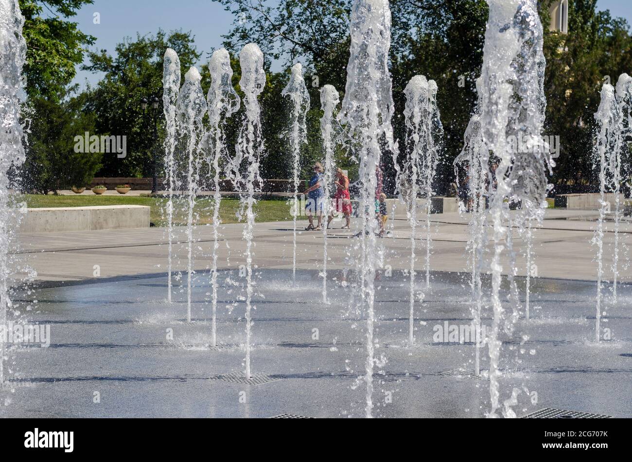Nikolaev, Ukraine - 17. August 2020: Die Bewohner flanieren neben den kühlen Bächen des Stadtbrunnens auf dem Stadtplatz. Jets von kühlem klarem Wasser Gushi Stockfoto