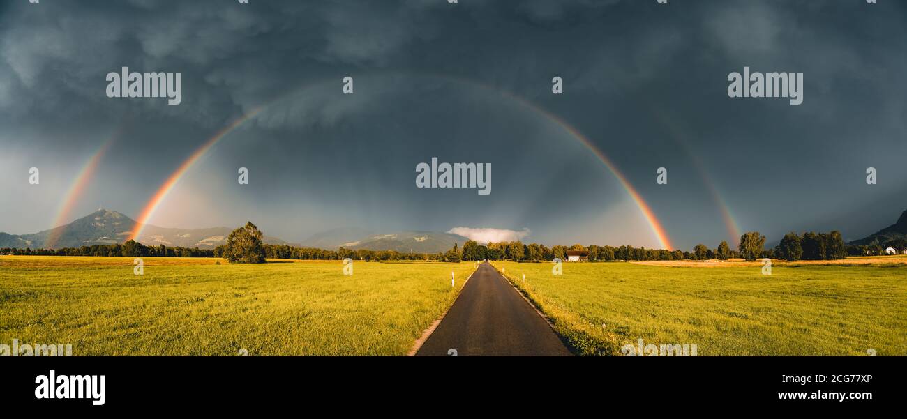 Doppelter Regenbogen über einer Straße durch ländliche Landschaft, Salzburg, Österreich Stockfoto