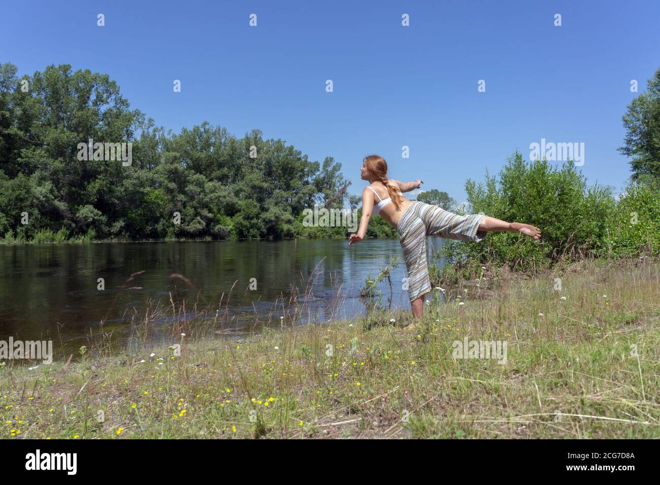 Rothaarige Mädchen macht Gymnastik am Ufer des Flusses vor einem Hintergrund von Bäumen, an einem sonnigen Sommertag. Stockfoto