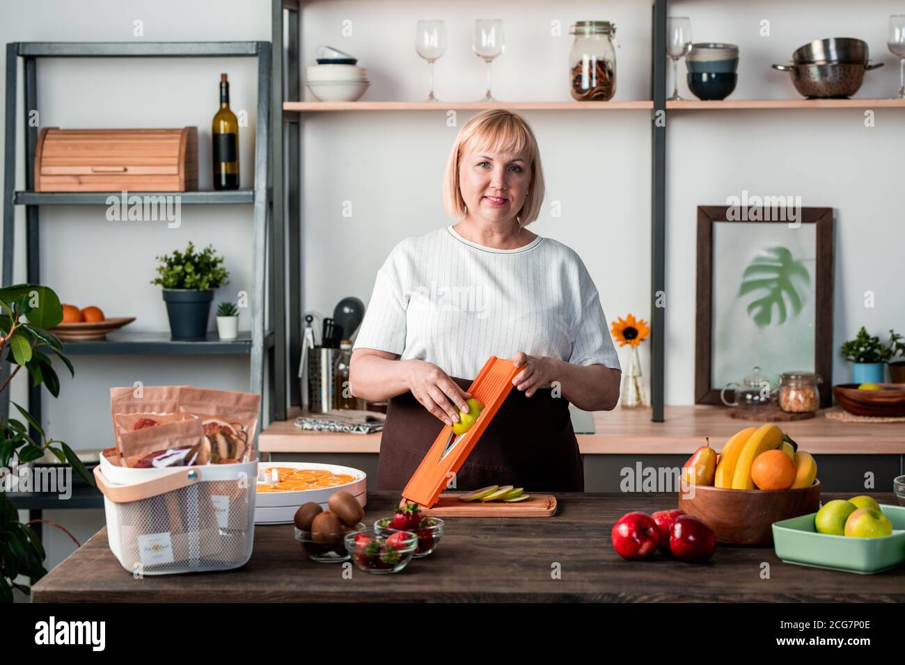 Portrait von lächelnden reifen Lebensmittel-Blogger an der Theke stehen und Verwenden von Slicer beim Kochen in der heimischen Küche Stockfoto