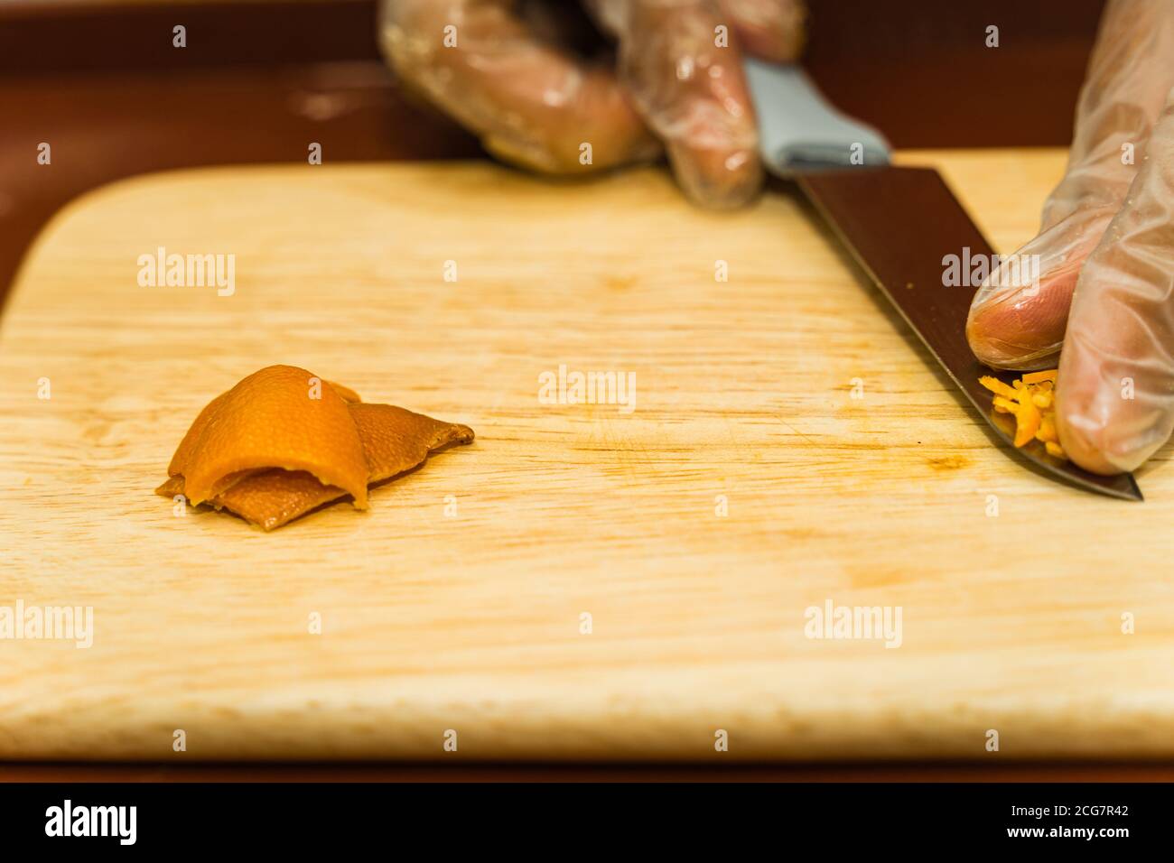 Eine Nahaufnahme der Hand einer Frau mit einem Messer geschnitten getrocknete Mandarine Schale auf einem hölzernen Schneidebrett. Food-Konzept Stockfoto