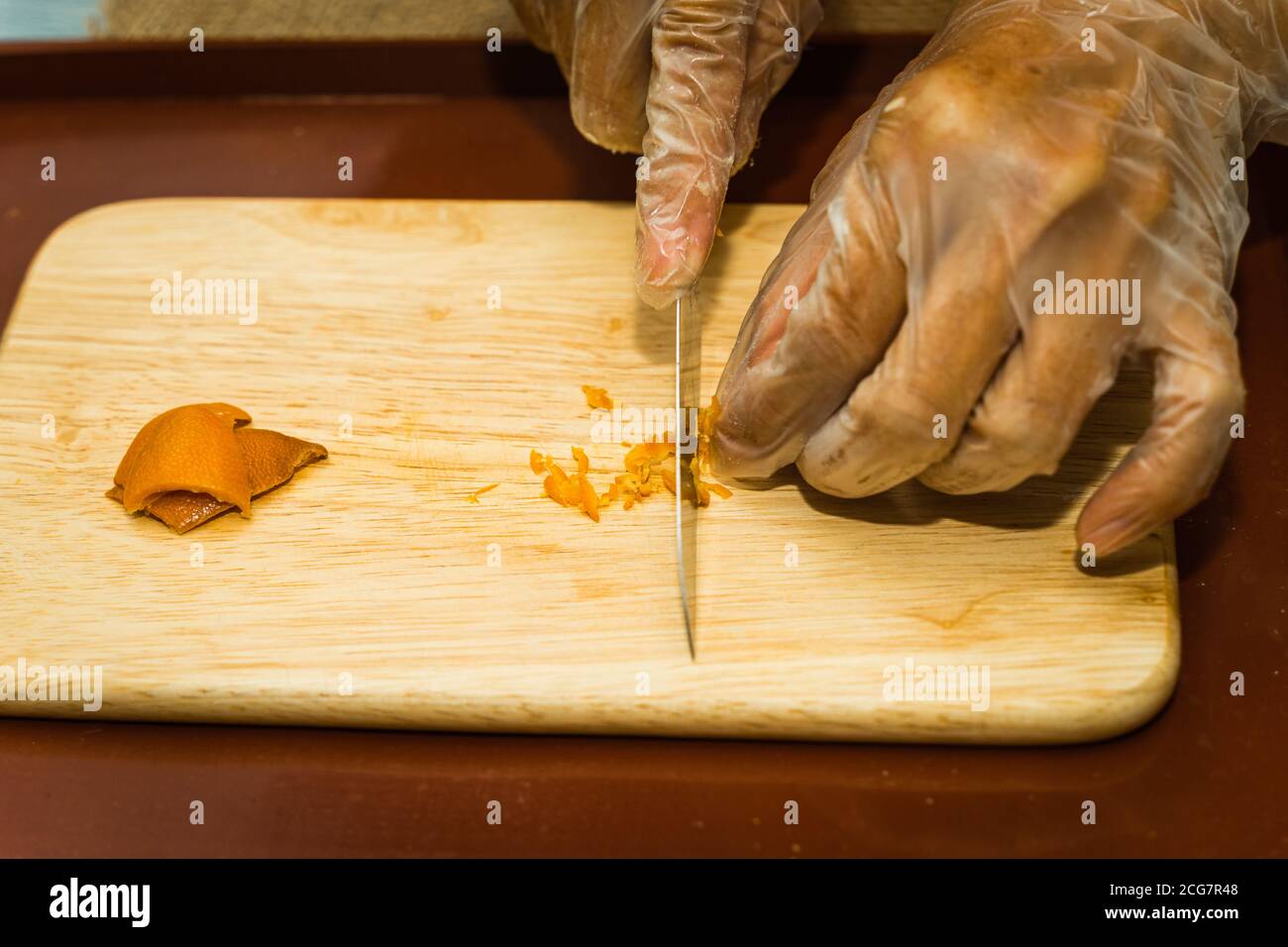 Eine Nahaufnahme der Hand einer Frau mit einem Messer geschnitten getrocknete Mandarine Schale auf einem hölzernen Schneidebrett. Food-Konzept Stockfoto