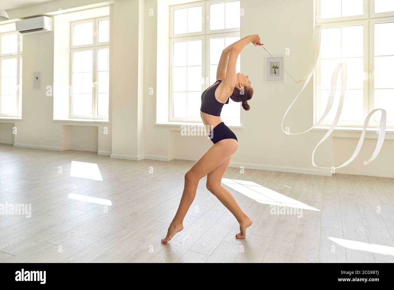 Anmutige junge Turnerin Mädchen mit weißem Band Proben Gymnastik Elemente In modernem Studio Stockfoto