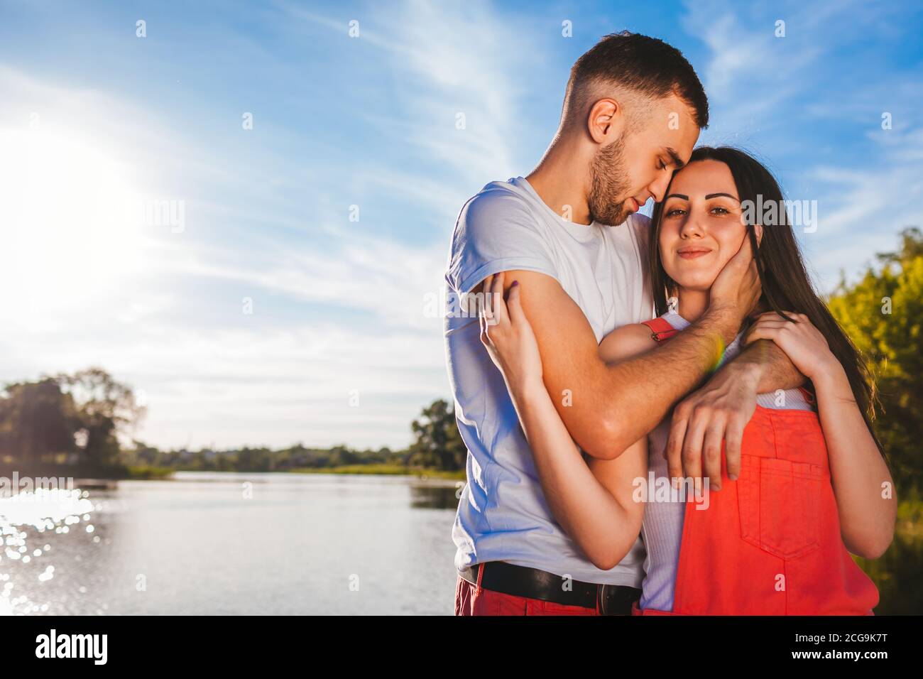 Glückliches Paar in der Liebe umarmt am Fluss bei Sonnenuntergang. Mann und Frau gehen draußen auf Datum Stockfoto