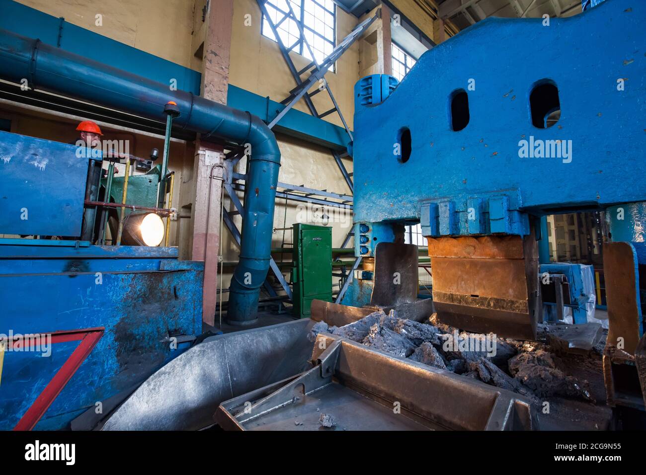 Zerkleinerungsmaschine für Titan-Schwamm in der Werkshalle. Metallurgiewerk. Maschinenbediener in orangefarbenem Hardhut pressen. Stockfoto