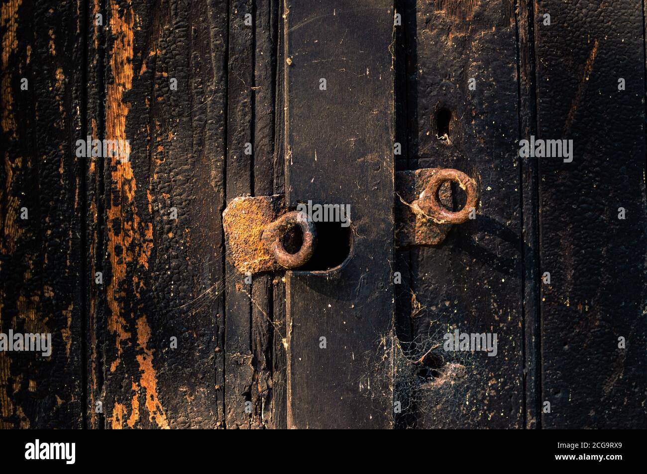 Rostige Augenschrauben an einer verbrannten Holztür beleuchtet Bei der Abendsonne Stockfoto