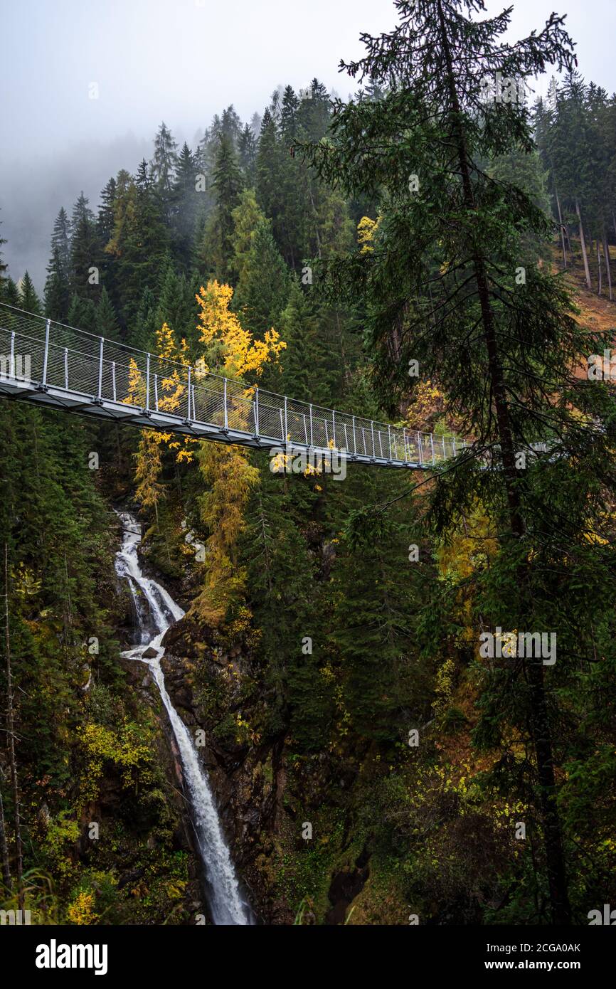 Hängebrücke aus Metall über dem schönen Rabby-Tal im Nebel irgendwo in Norditalien im Frühherbst. Stockfoto