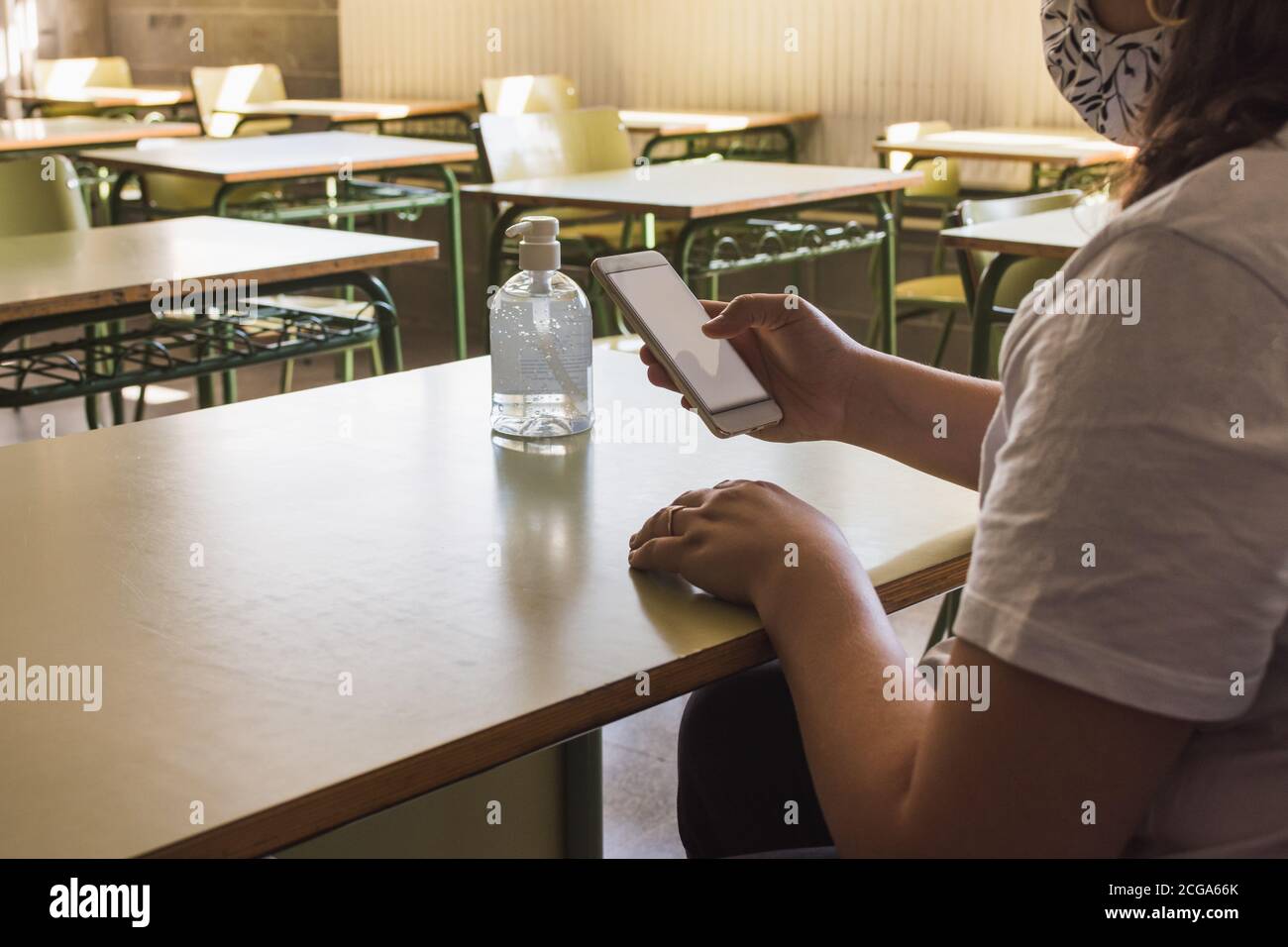 Lehrerin mit Gesichtsmaske überprüft ihr Smartphone während der Wartezeit Ihre Schüler zu lehren Stockfoto