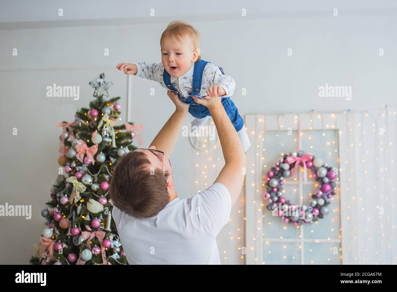 Junger Vater wirft Baby Sohn in hellen weißen Raum mit Weihnachten Interieur zu Hause. Familie, Urlaub, Elternschaft, Spiel, Kindheit und Stockfoto