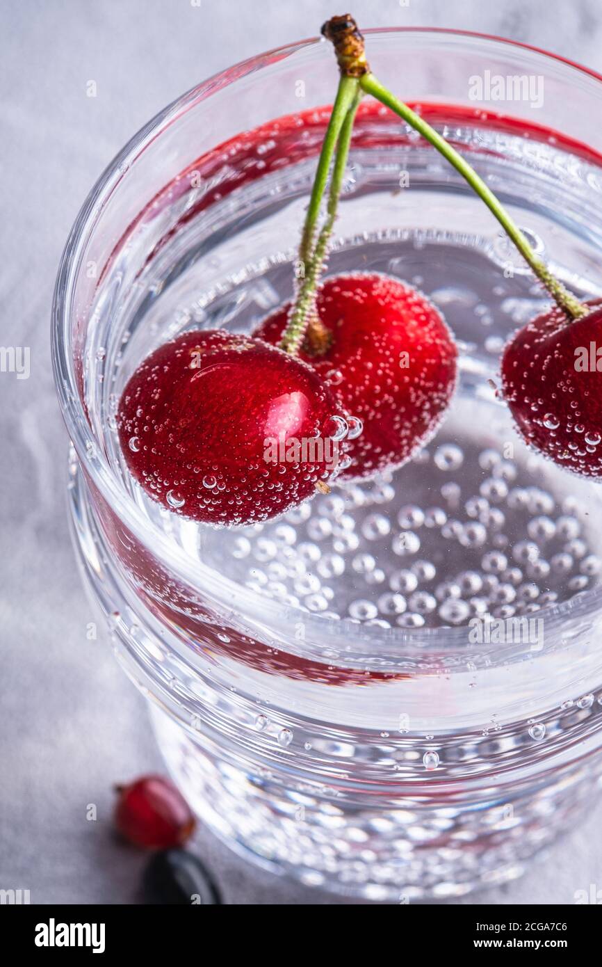 Frisches kaltes Mineralwasser Getränk mit Kirsche, Himbeere und Johannisbeere in transparentem Glas auf Steinbeton Hintergrund, sommerliche Diät Getränk Stockfoto