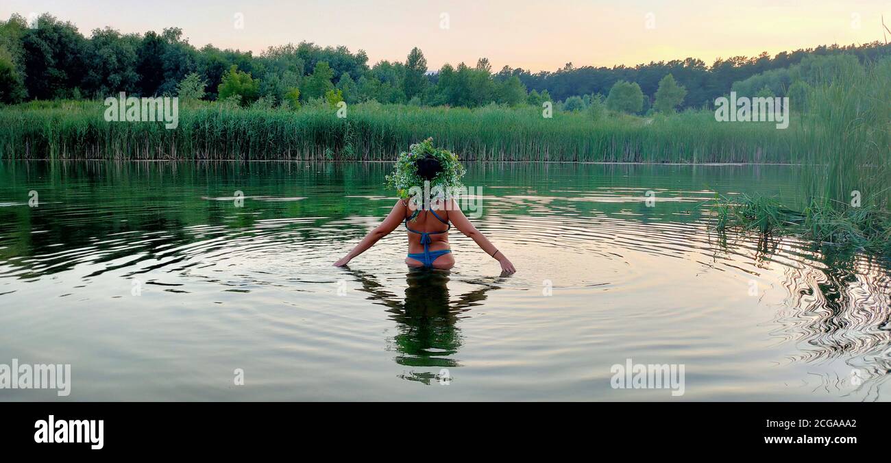 Ein Mädchen in einem Badeanzug und mit einem Blumenstrauß auf dem Kopf, steht im Wasser im Urlaub von Ivan Kupala Stockfoto