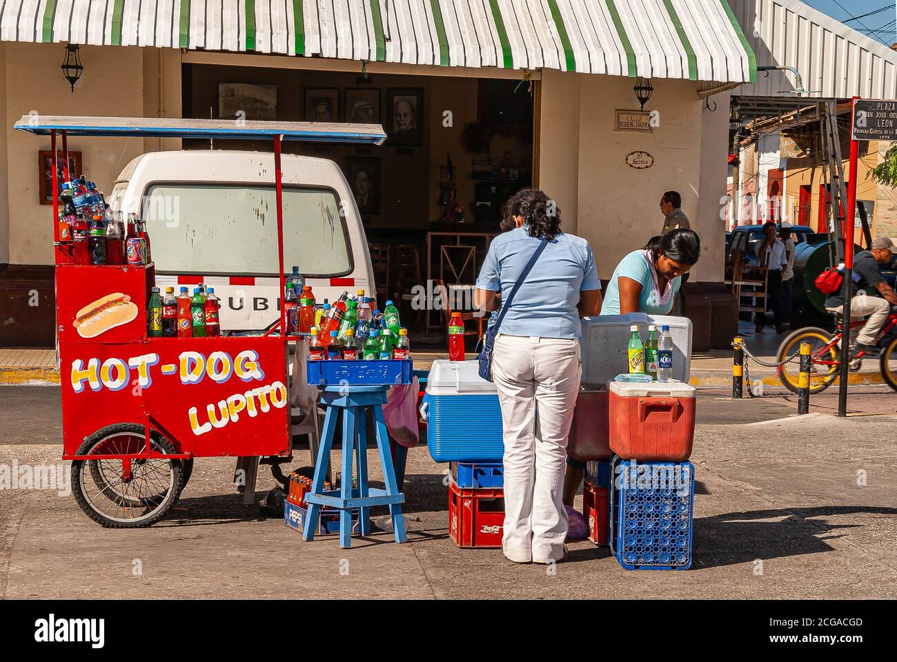 Leon, Nicaragua - 27. November 2008: Schirmherr vor rotem Hot-Dog und Getränkewagen mit Verkäufer vorhanden und vielen Flaschen auf dem Display vor E Stockfoto