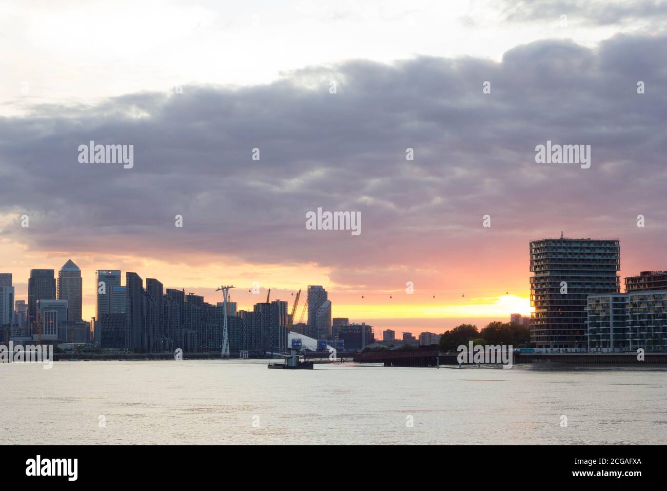 Warme Sonnenstrahlen brechen durch dicke und dunkle Sonnenuntergangswolken über Canary Wharf Skyline, Themse East London England Stockfoto