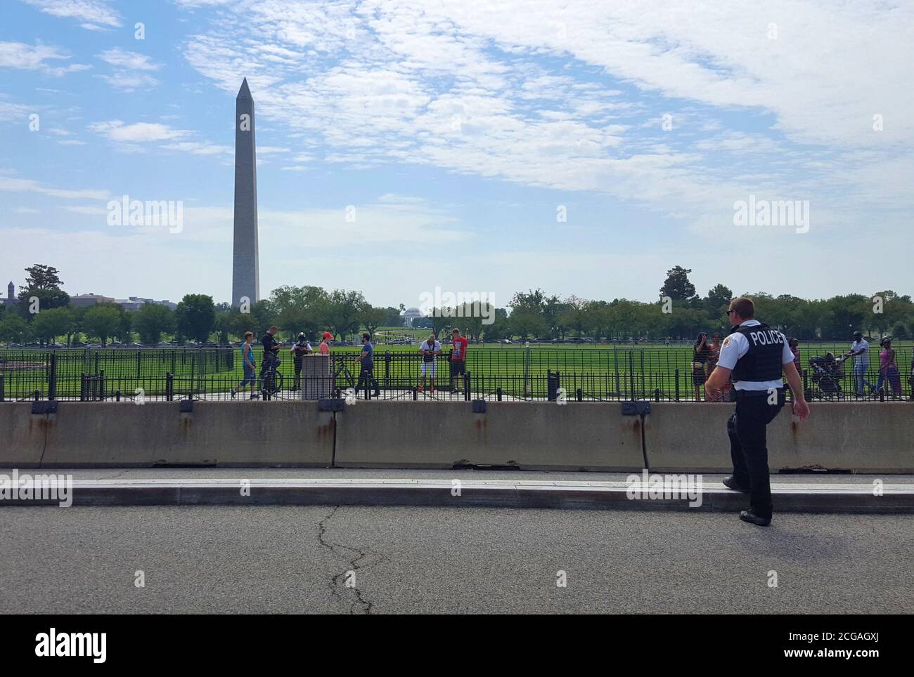 Ein Washington D.C. Polizist, der die Straße mit dem Washington Monument in der Ferne überquert, Washington D.C., USA Stockfoto
