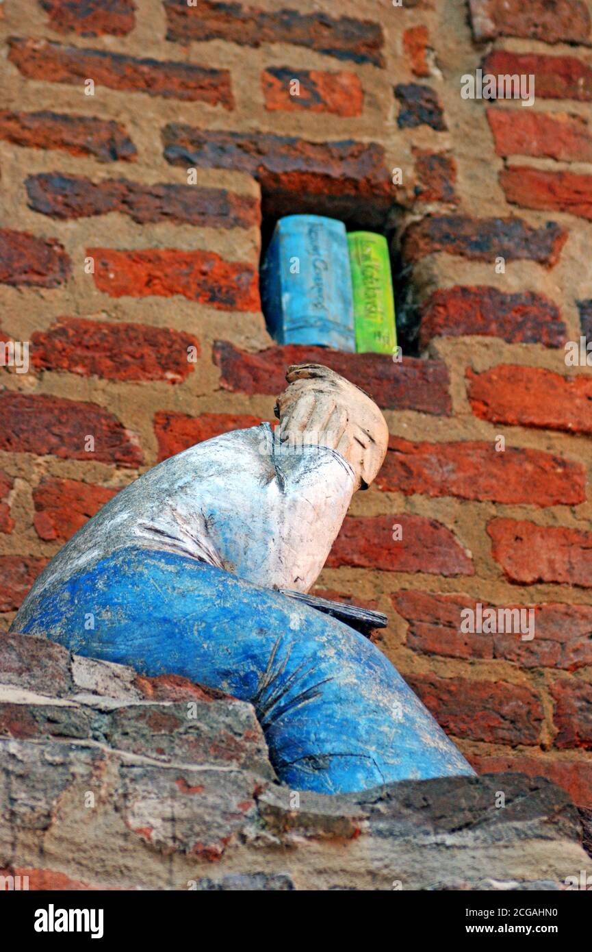 Ein Lehmmännchen sitzt in einer kontemplativen Position mit Büchern in der Nähe in der Backsteinmauer in der Altstadt von Torun, Polen. Stockfoto