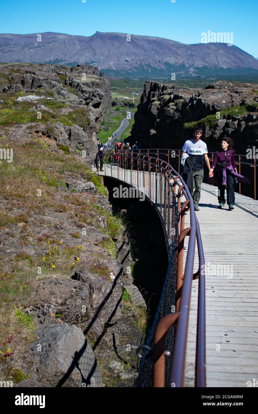 Zwei Besucher gehen die hölzerne Promenade zwischen einem der Haltepunkte in den Felsen, die durch die kontinentale Verschiebung geschaffen wurden, Thingvellir Nationalpark hinauf. Stockfoto