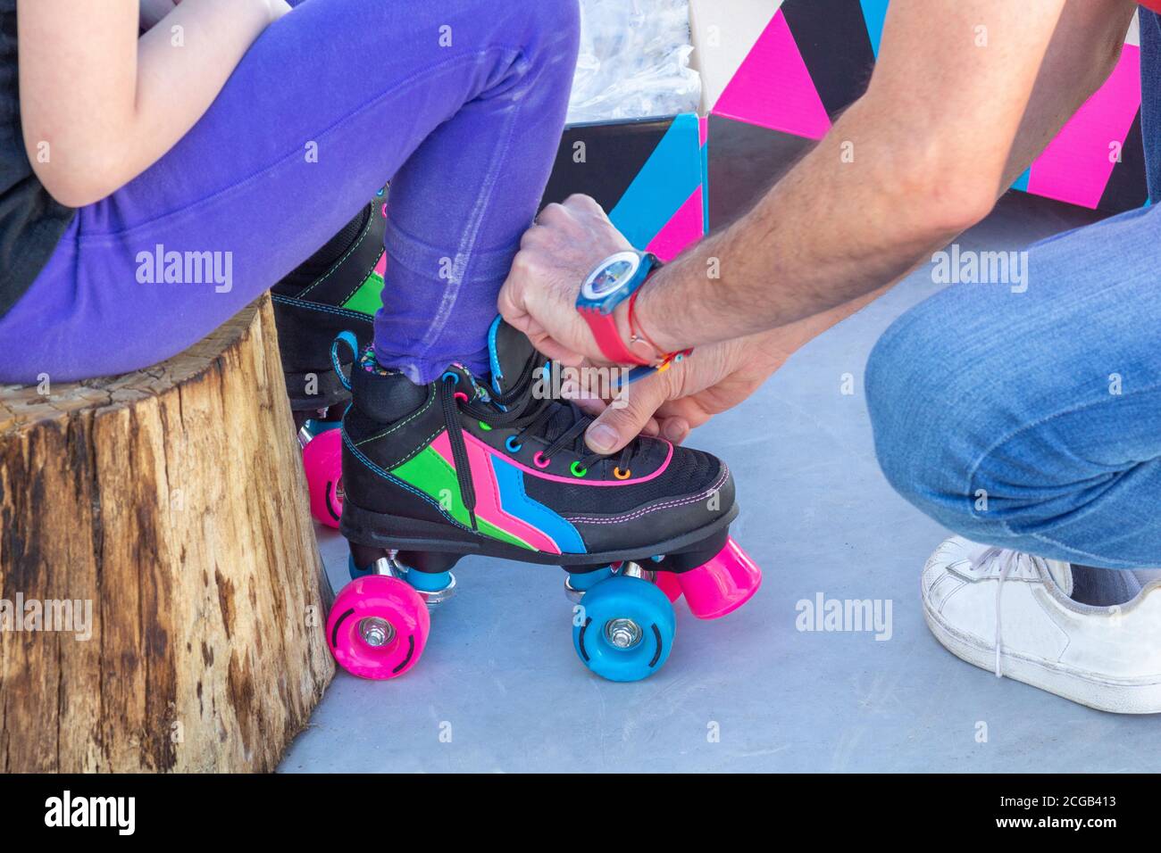 Nahaufnahme eines Vaters, der Rollschuhe auf seine Tochter legt, man kann ihre Gesichter nicht sehen Stockfoto