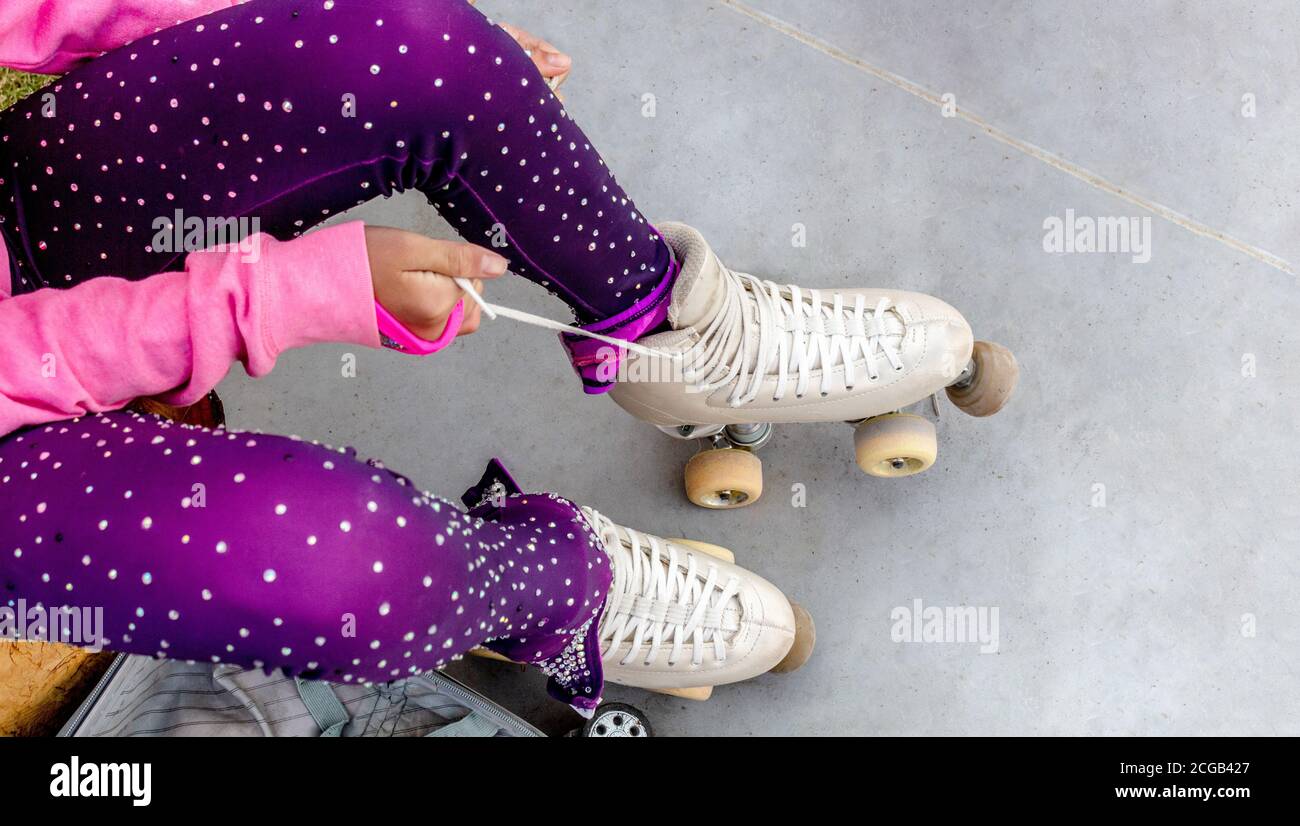 Beine einer Skaterin, die die Schnürsenkel ihrer Rollschuhe bindet. Sie ist in einem Eiskunstlauf-Glanzanzug Stockfoto