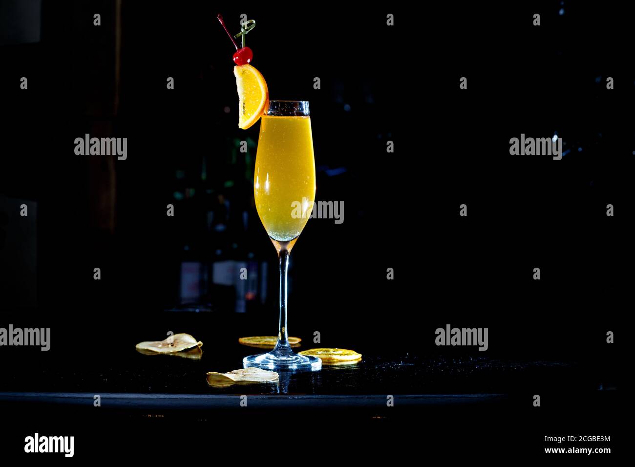 Ein gelber Cocktail in einem hohen Weinglas steht auf der Theke einer dunklen Bar. Stockfoto