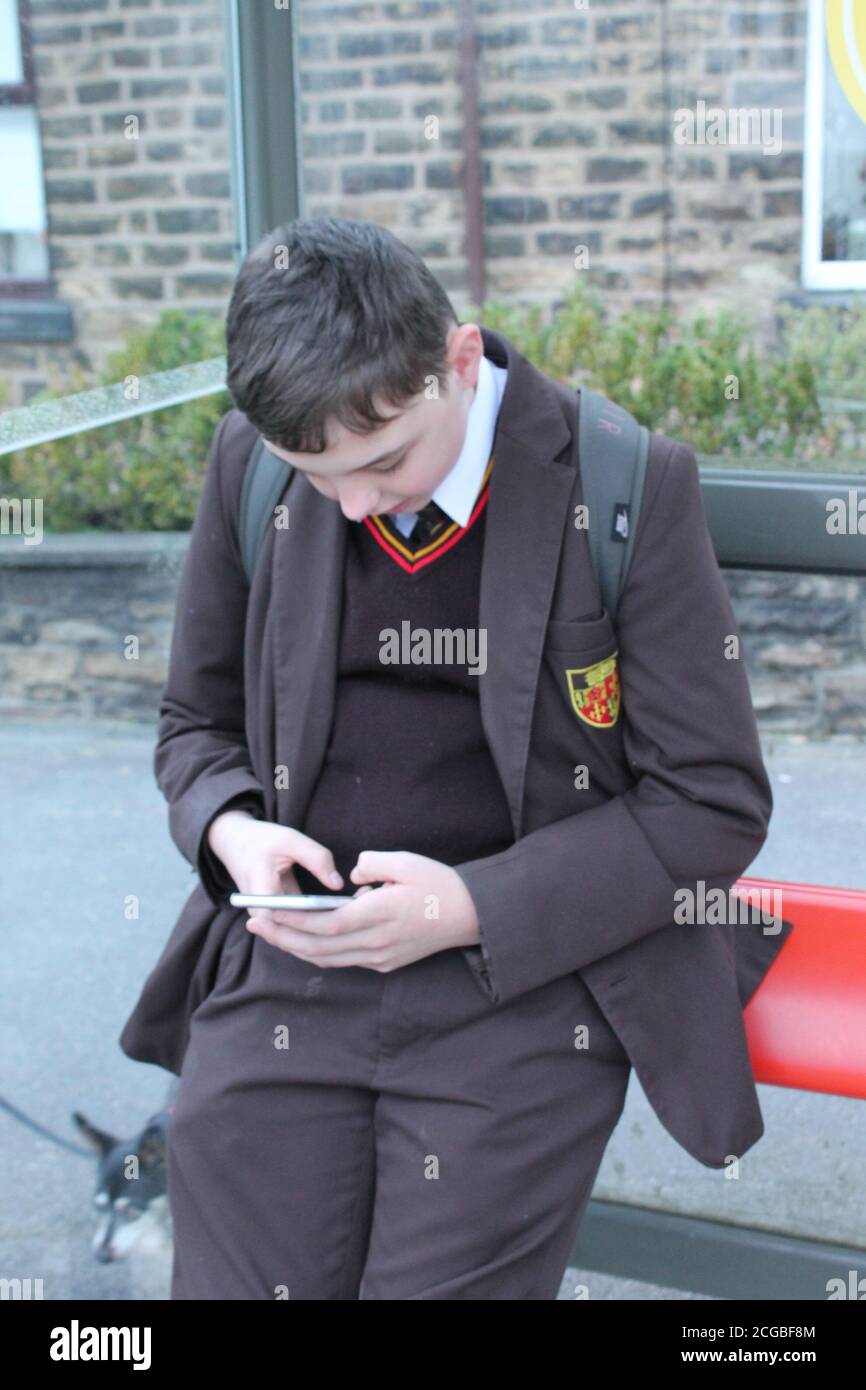 Teenager-Schuljunge in brauner Schuluniform schaute nach unten und setzte sich mit SMS auf ein Mobiltelefon Stockfoto