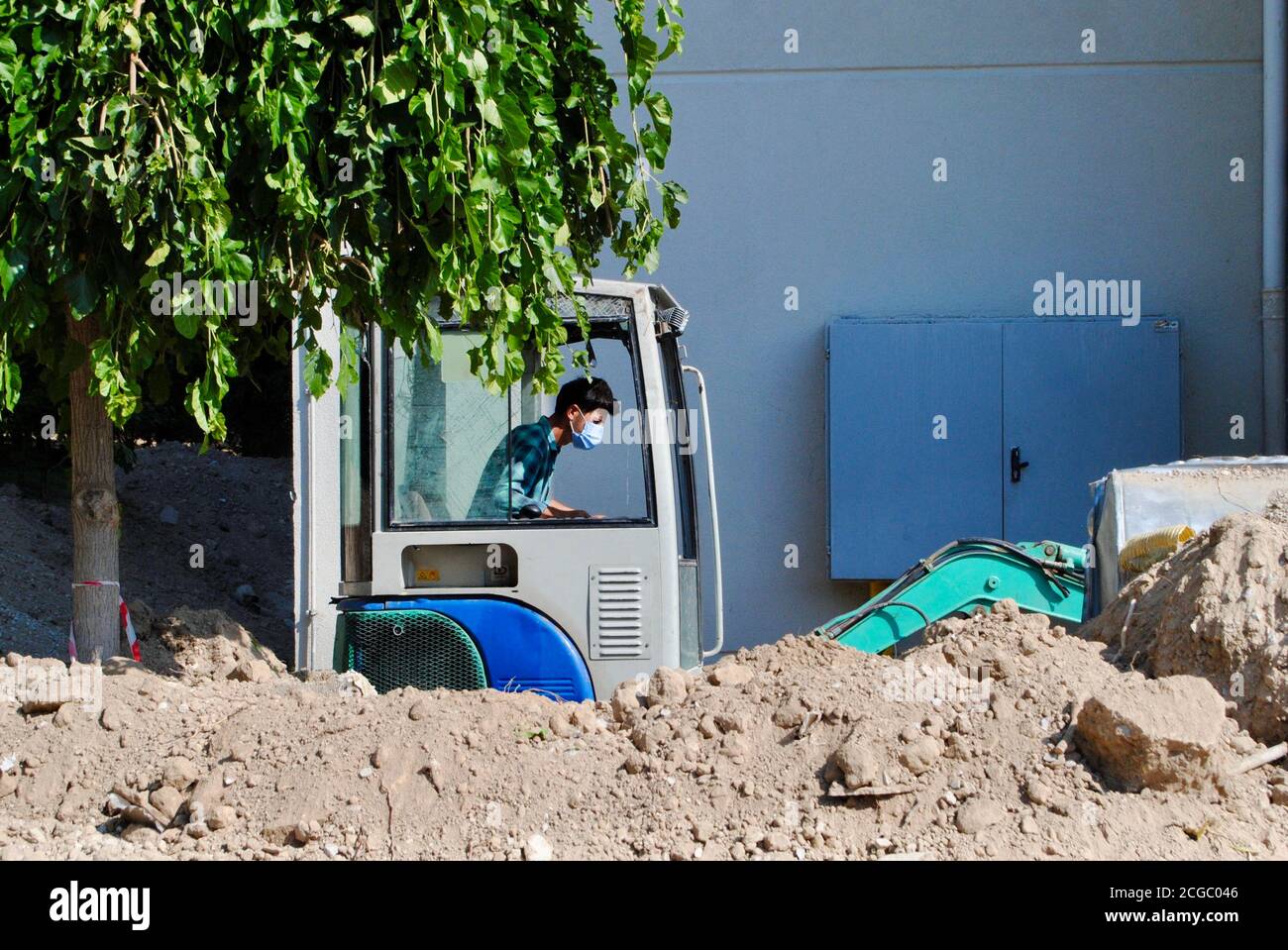 Bauarbeiter mit Maske, die während der Covid-19-Ära den Bulldozer auf der Baustelle bediente. Covid-19-Inhalt Stockfoto