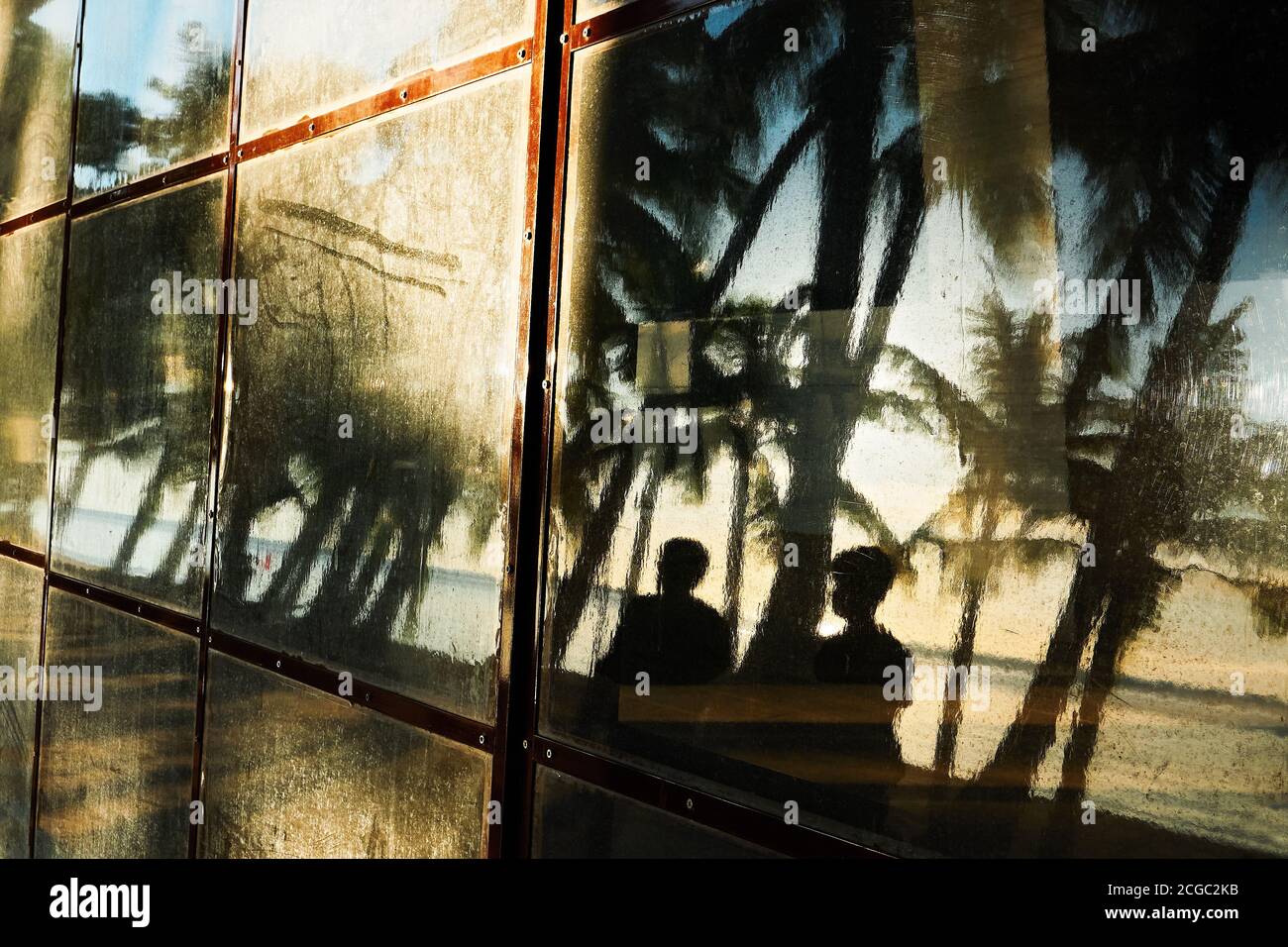 Abstraktes Foto einer Reflexion von zwei Personen, die am späten Nachmittag an der Strandpromenade spazieren. Hemmnisse schließen Geschäftsbetriebe, weil Corona Stockfoto