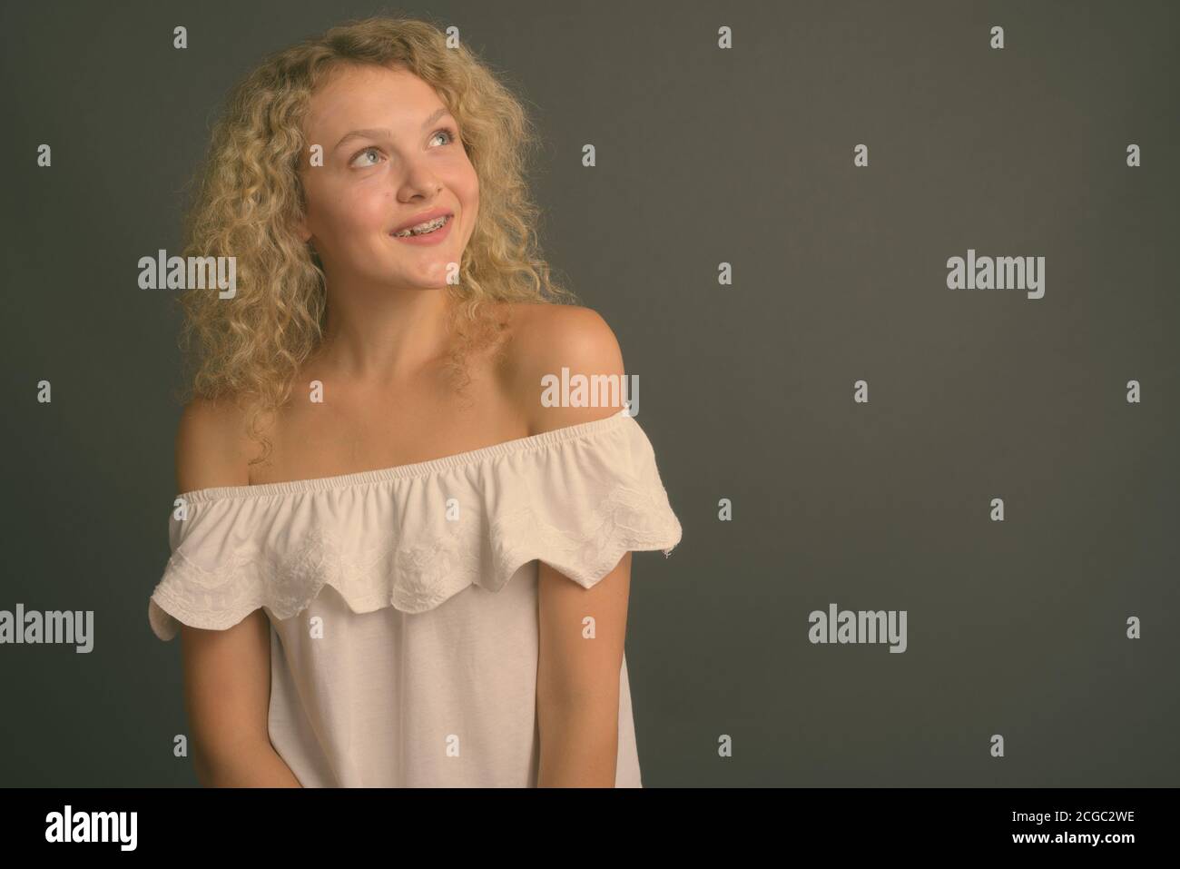 Junge schöne Frau mit blondem lockiges Haar vor grauem Hintergrund Stockfoto