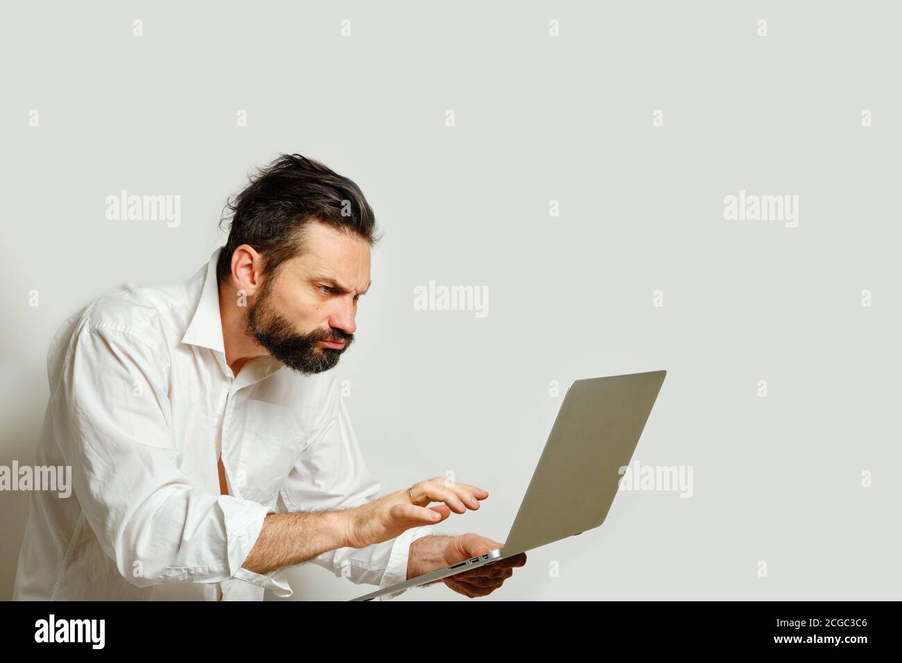Kaukasischen Mann suchen mit Unmut wütend in Laptop-Monitor isoliert auf grauem Hintergrund. Seitenansicht. Menschliche Emotionen, Gesichtsausdruck Konzept Stockfoto